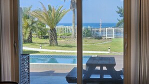Una habitación con puerta corrediza de vidrio que da a una zona de piscina con vista al océano y palmeras.