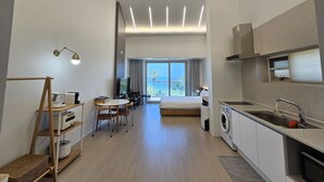 Una habitación de hotel moderna con kitchenette, comedor, una cama grande y vista al mar.