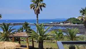 Vista de una playa con un quiosco de madera, palmeras y una costa rocosa.