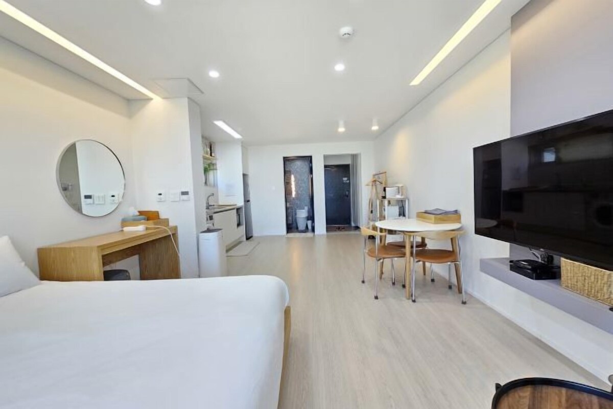 Quarto de hotel moderno com cama, escrivaninha, televisão e área de refeições.