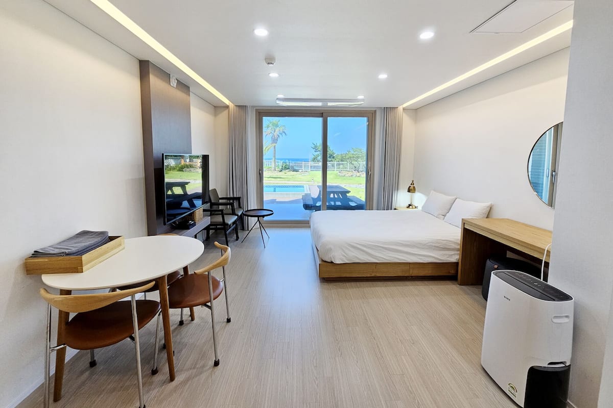 A hotel room with a bed, a desk, a TV, a dining table, and a view of the outdoors.