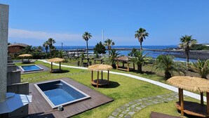 Un área de piscina con vista al océano, palmeras y un pabellón.
