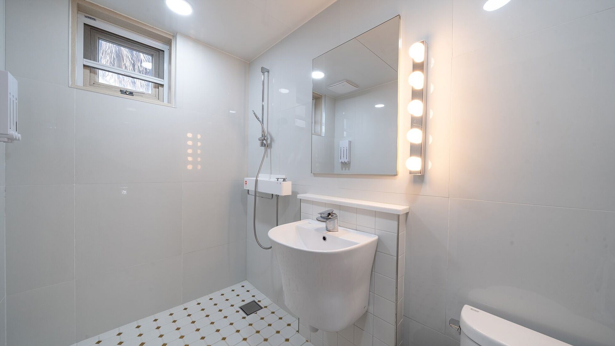 Un bany modern amb un lavabo blanc, un mirall amb il·luminació i una dutxa.