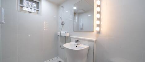 Un bany modern amb un lavabo blanc, un mirall amb il·luminació i una dutxa.