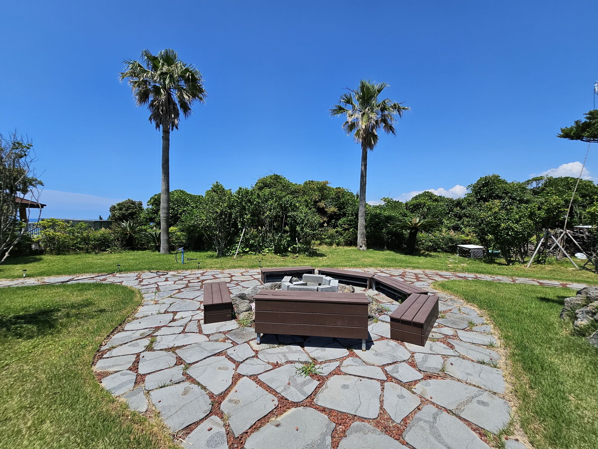 A stone patio with a circular seating area, surrounded by grass and palm trees.