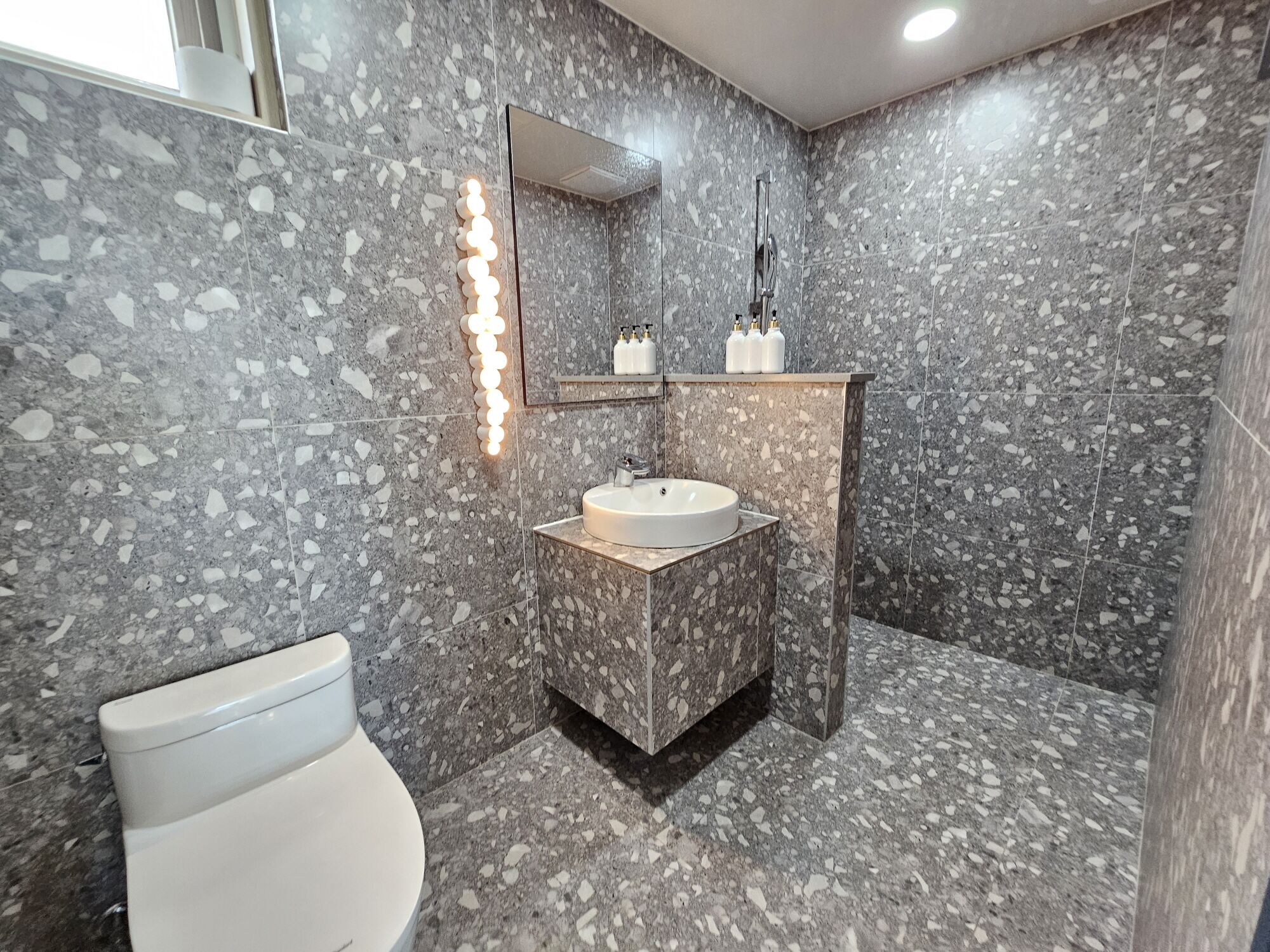 A modern bathroom with a marble floor, a round sink, a toilet, and a mirror with a light strip.
