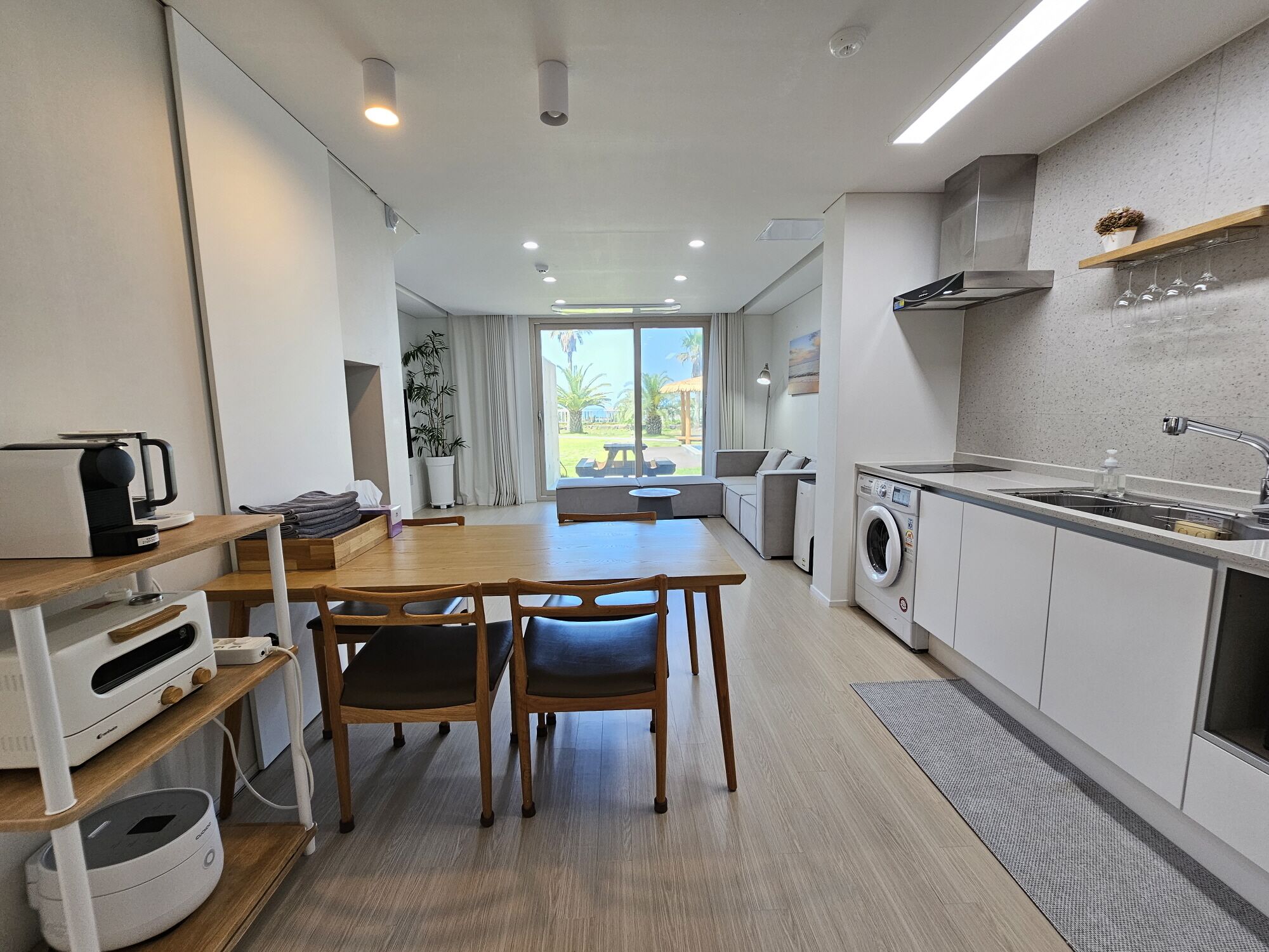 A modern kitchen with a dining area, a washing machine, and a view of the outdoors.