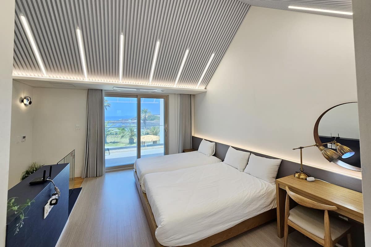 A modern hotel room with a large bed, a desk, and a view of the sea.