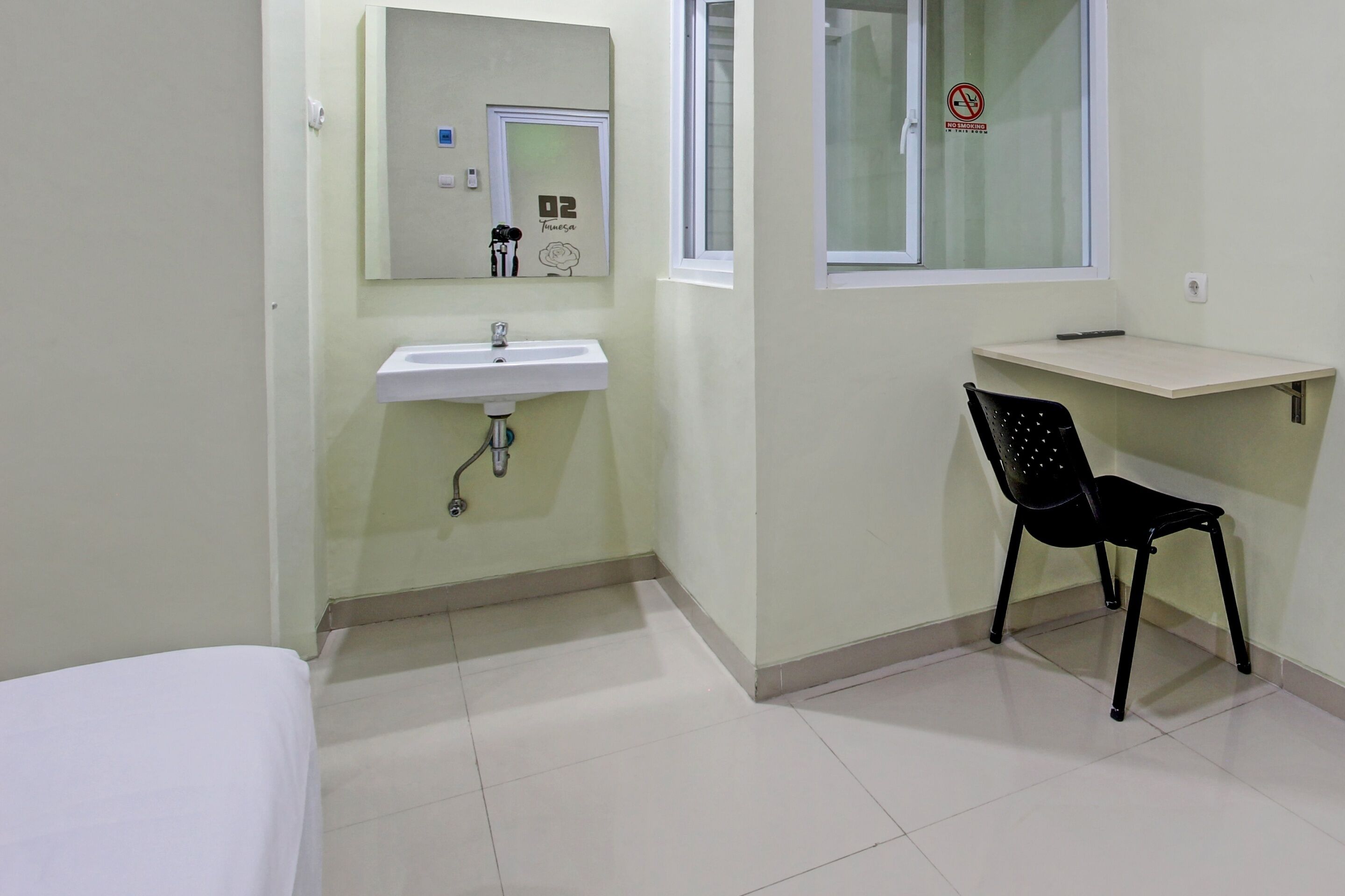 A small, clean room with a white sink, a mirror, a window, and a black chair.