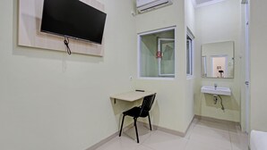 Ein Zimmer mit einem Wand-Fernseher, einem Schreibtisch mit Stuhl, einem Fenster mit Verbotsschild und einem Waschbecken sowie einer Klimaanlage.