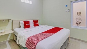 Ein ordentlich bezogenes Bett mit roter und weißer Bettwäsche, ein Nachttisch mit einem weißen Handtuch und ein Fenster mit floralem Dekor.