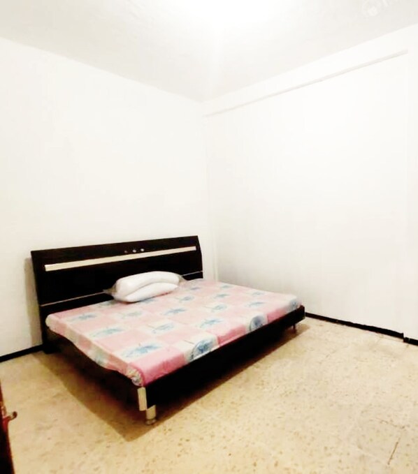 A small, single-bed room with a wooden headboard and a pink bedspread.