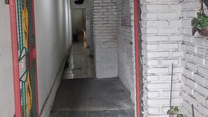 A narrow hallway with white brick walls, a red door frame, and a tiled floor. - Hotel O Onong's Homestay Near Dodikjur Rindam XIII/Merdeka (Tomohon)
