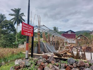 A construction site with a sign for Onong's Homestay & Cafe, bamboo structures, and a red building in the background. - Hotel O Onong's Homestay Near Dodikjur Rindam XIII/Merdeka (Tomohon)
