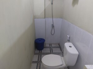 A small bathroom with a toilet, a shower, and a blue trash bin. - Hotel O Onong's Homestay Near Dodikjur Rindam XIII/Merdeka (Tomohon)