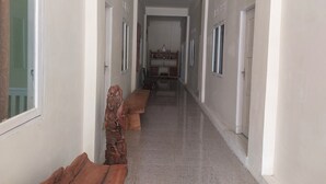 A hallway with white walls, a polished floor, and wooden benches on one side. - Hotel O Onong's Homestay Near Dodikjur Rindam XIII/Merdeka (Tomohon)