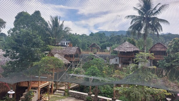 A rustic outdoor area with thatched-roof huts, a patio with wooden furniture, and lush greenery. - Hotel O Onong's Homestay Near Dodikjur Rindam XIII/Merdeka (Tomohon)
