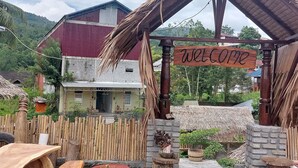 A rustic wooden structure with a 'Welcome' sign, surrounded by a bamboo fence, a thatched roof, and a brick wall. - Hotel O Onong's Homestay Near Dodikjur Rindam XIII/Merdeka (Tomohon)