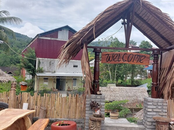 A rustic wooden structure with a 'Welcome' sign, surrounded by a bamboo fence, a thatched roof, and a brick wall. - Hotel O Onong's Homestay Near Dodikjur Rindam XIII/Merdeka (Tomohon)