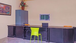 Ein Empfangsschalter mit einem grünen Stuhl, einem gerahmten Bild, einem Topfpflanze und einem Fernseher.