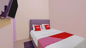 Ein Hotelzimmer mit einem Bett, einem an der Wand montierten Fernseher und einer rot-weißen Bettdecke.