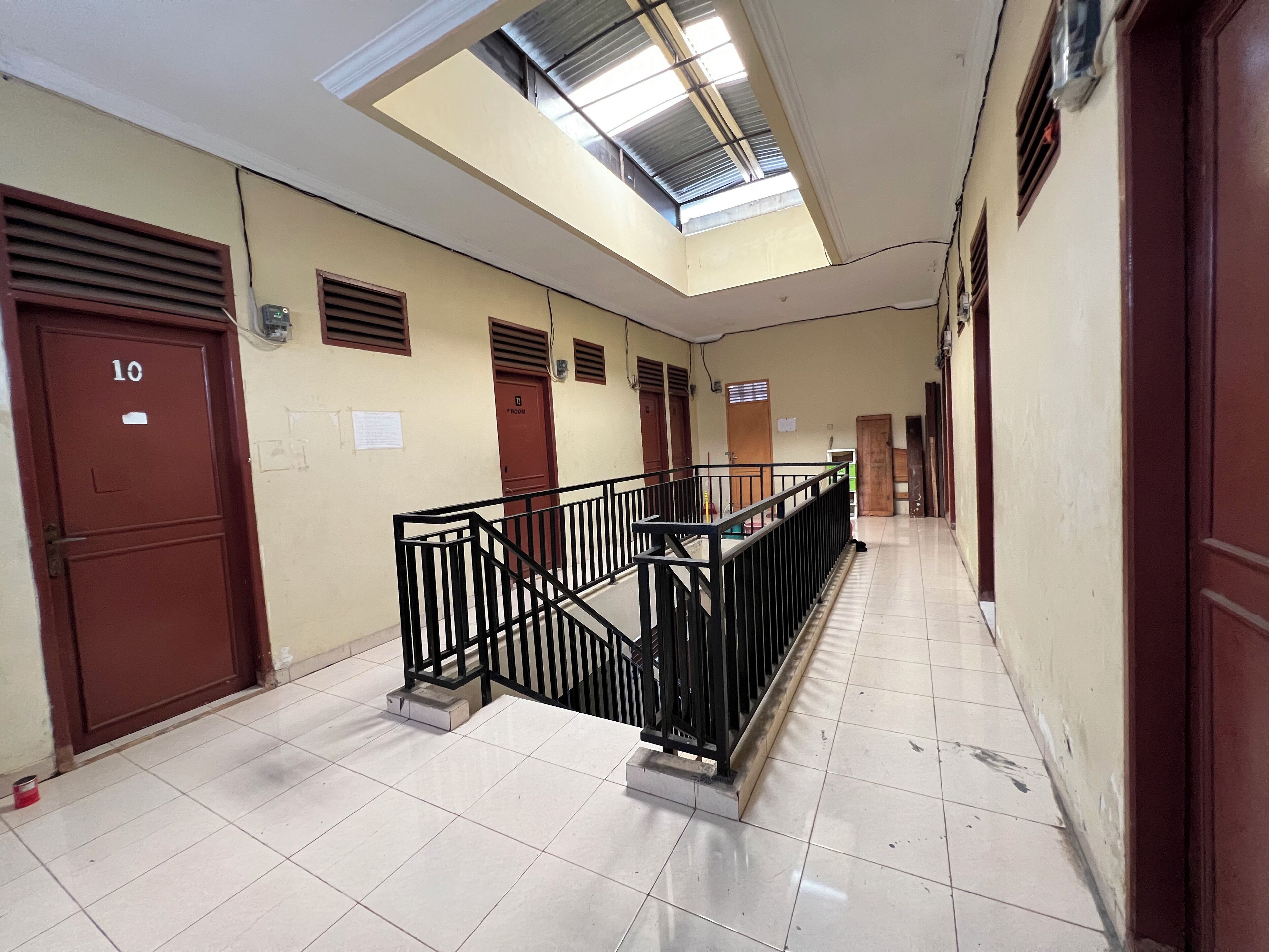 A corridor with a skylight, a staircase with a black railing, and doors labeled with room numbers.