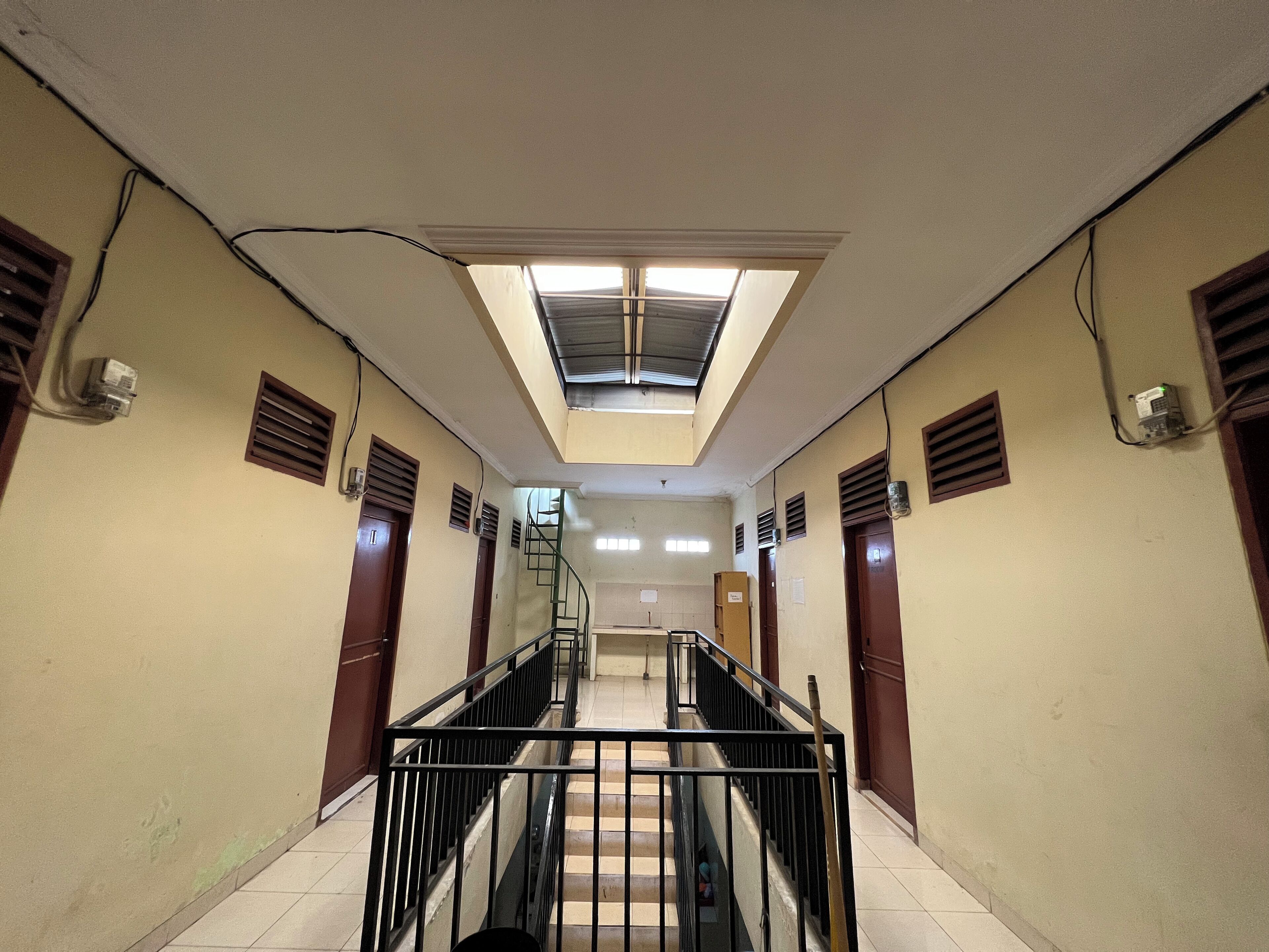 A corridor with a skylight, ventilation grills, and a staircase with a metal railing.