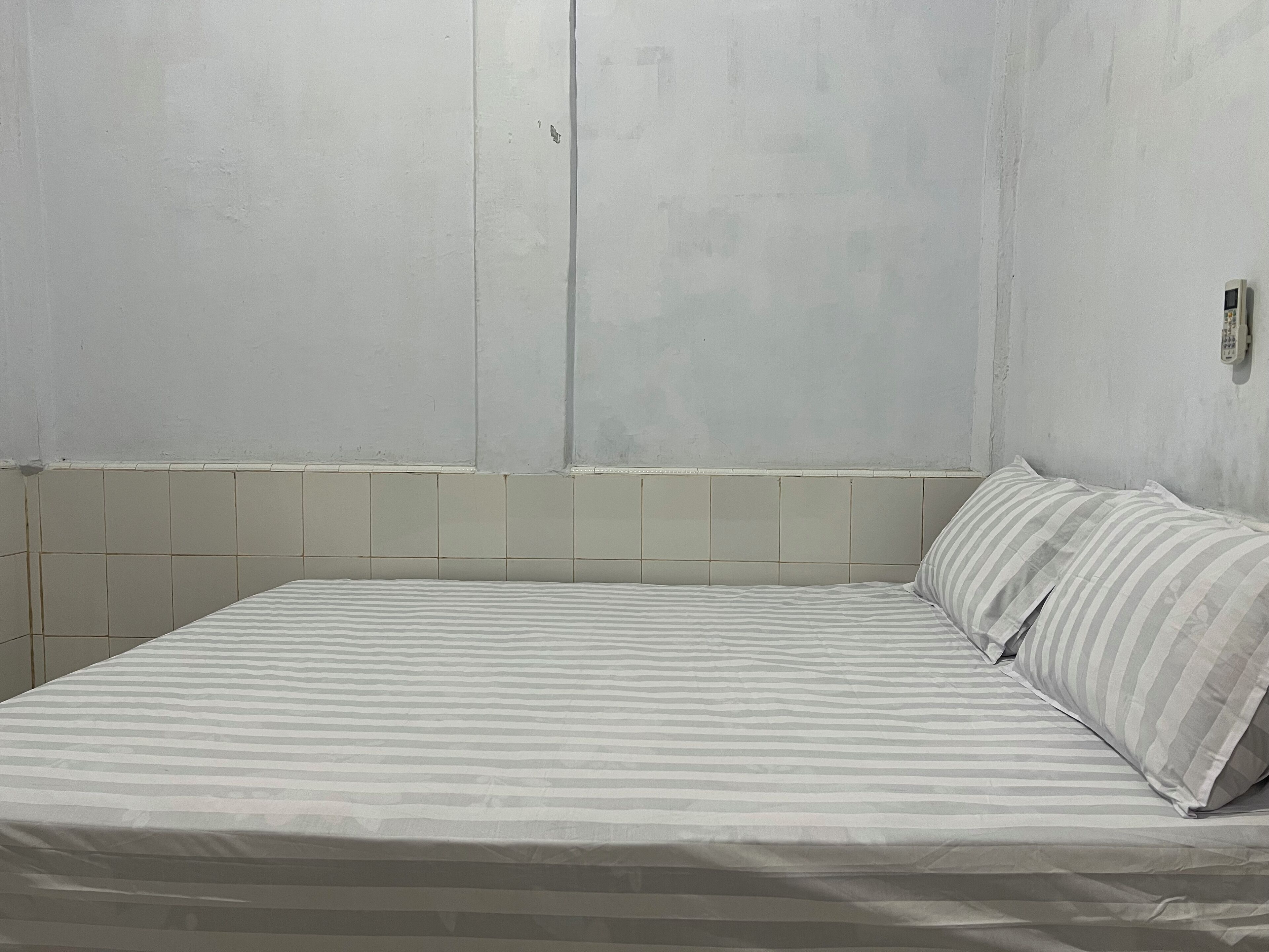A small, single-bed room with a plain white wall and a tiled lower section.