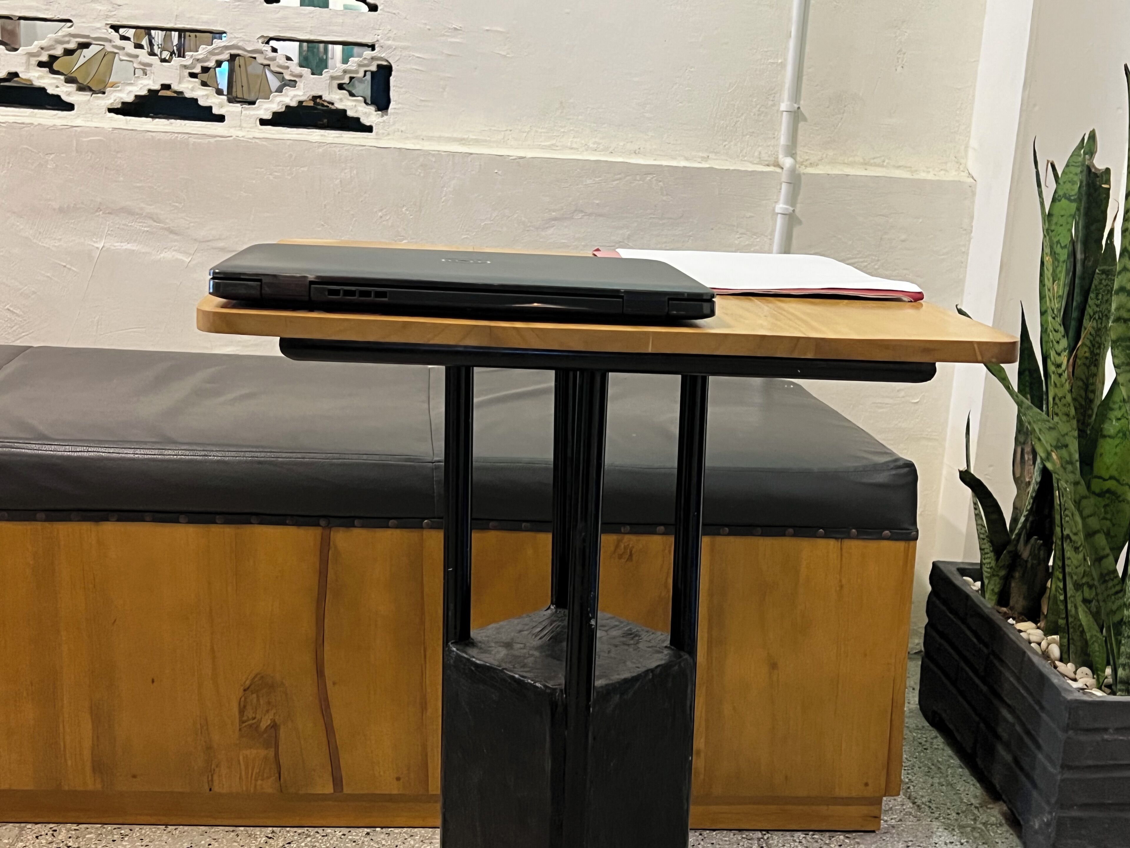 Una mesa de madera con una computadora portátil y una libreta, una silla negra y una planta en maceta.