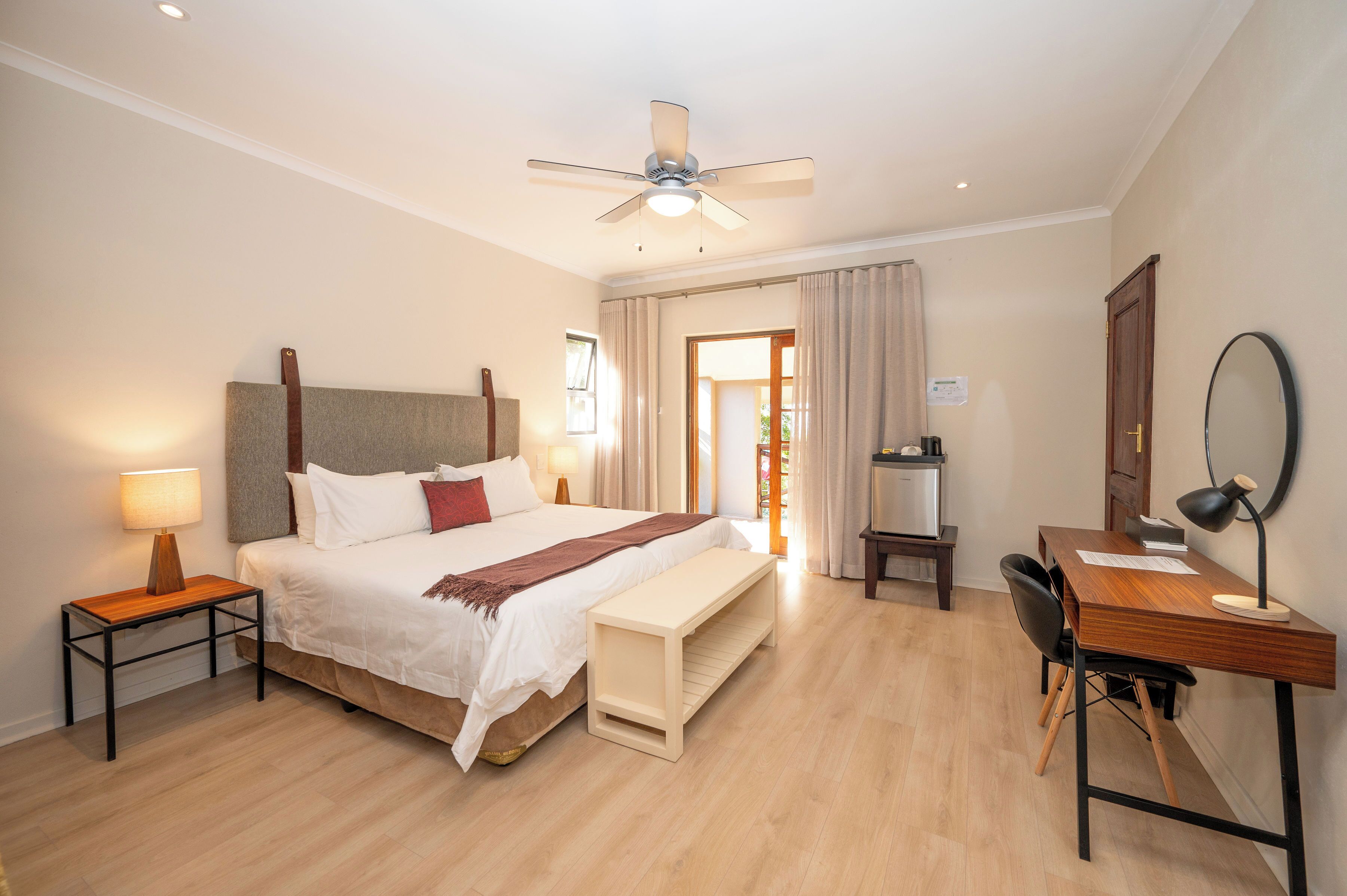 A hotel room with a bed, bedside tables, a desk, a chair, a ceiling fan, and a door leading to the bathroom.