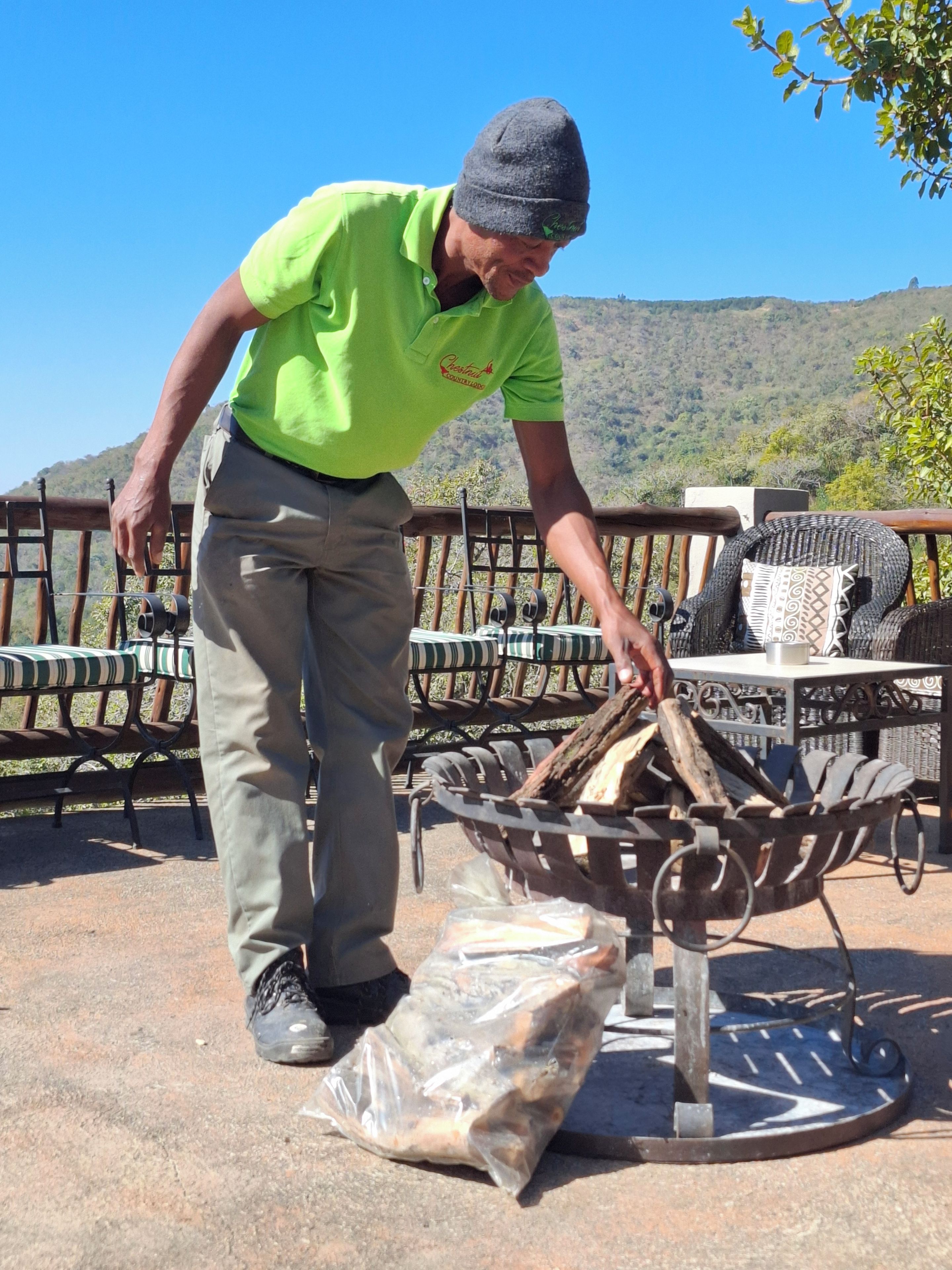 A person arranging firewood on a metal rack outdoors with a scenic view of hills in the background.