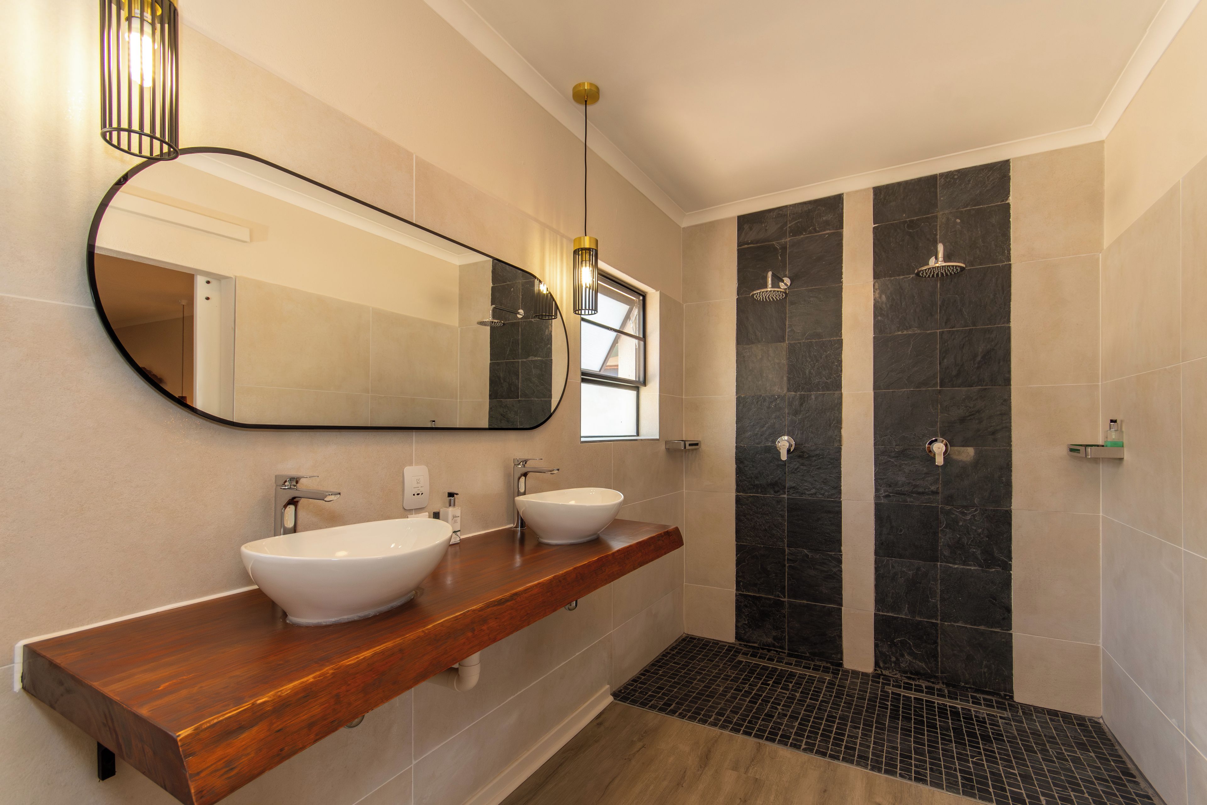 A modern bathroom with two sinks, a large mirror, and a shower area.