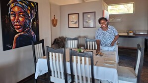 Een eetgedeelte met een tafel gedekt voor twee personen, stoelen, een decoratie van een pauwenveer en kunstwerken in lijsten aan de muur.