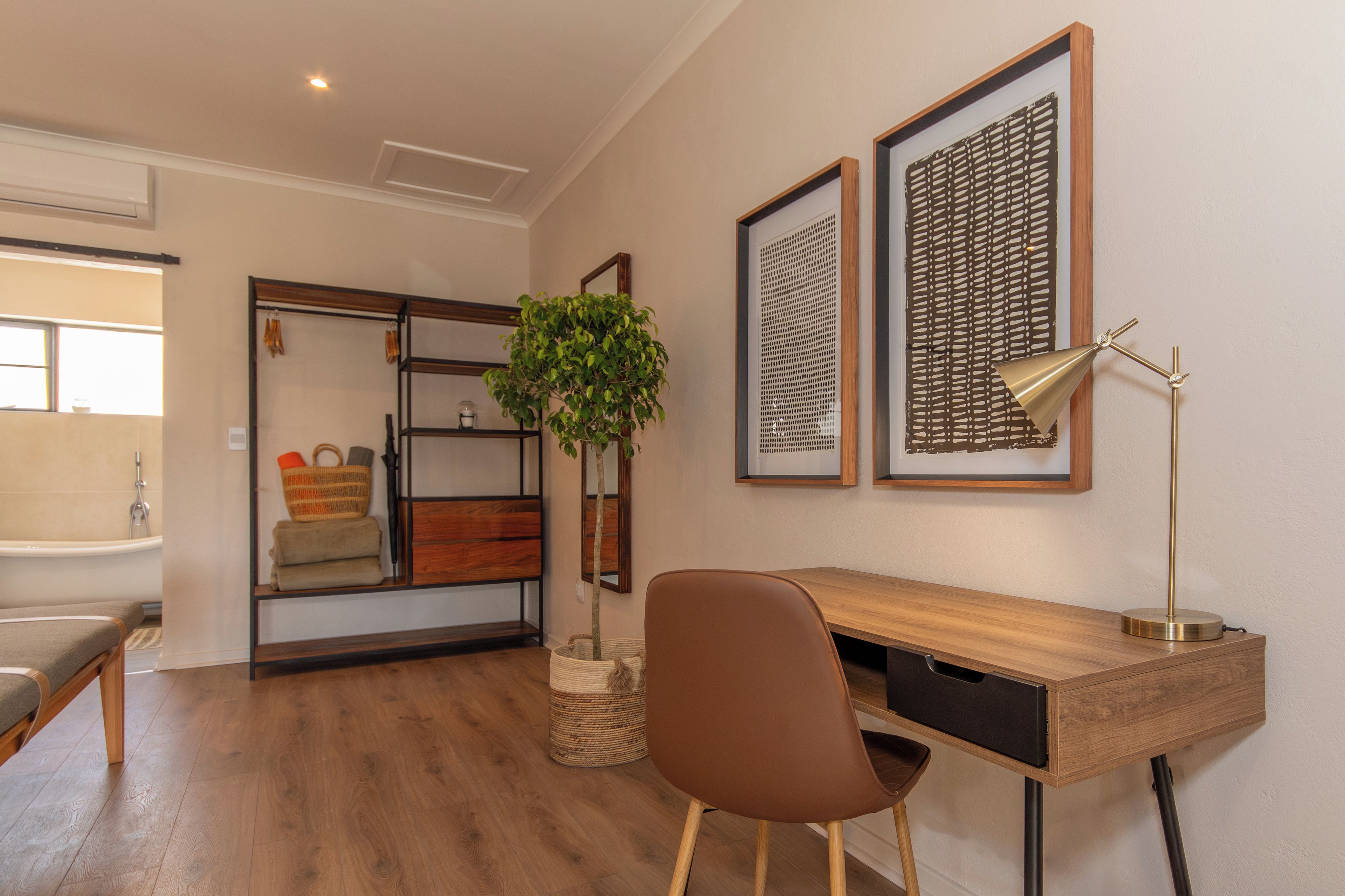 Una habitación moderna con un escritorio de madera, una silla marrón, una planta en maceta y cuadros en la pared.