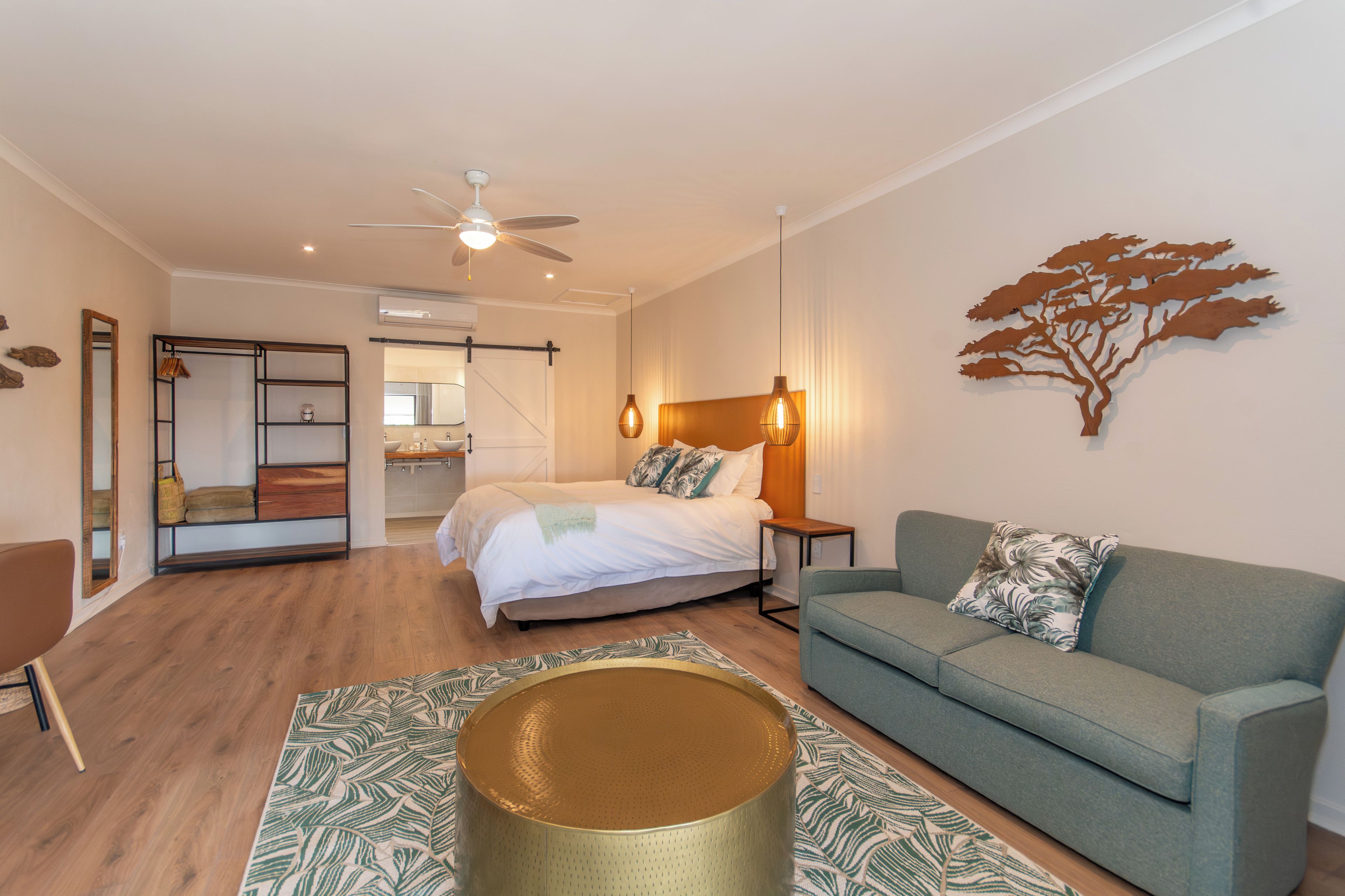 A modern bedroom with a bed, a seating area with a sofa, a standing lamp, and a decorative tree wall piece.