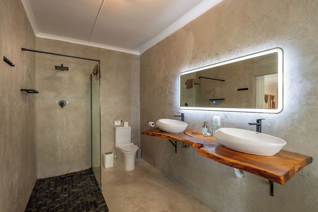 Ein modernes Badezimmer mit Duschkabine aus Glas, Toilette und Waschtisch mit zwei Becken und einem großen Spiegel.