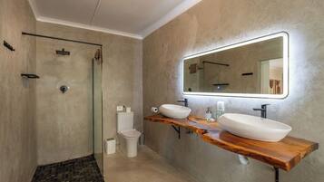 Een moderne badkamer met een glazen douchecabine, toilet en een wastafelmeubel met twee wasbakken en een grote spiegel.