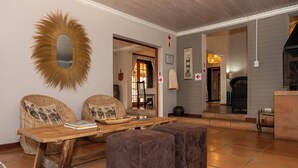Un salon avec des meubles en osier, une table en bois et un miroir. On y trouve deux poufs et un fauteuil avec des coussins.