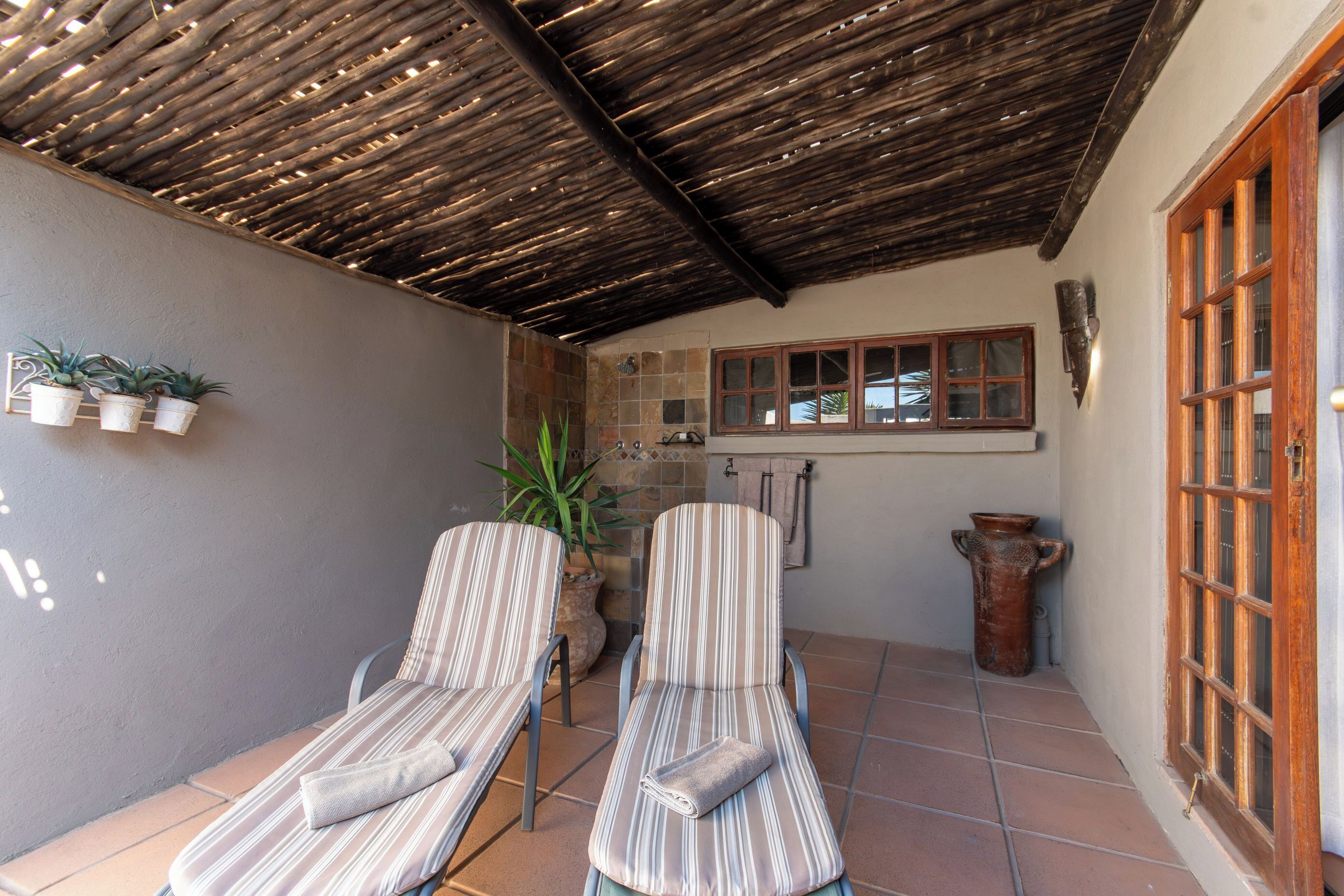 Une terrasse couverte avec deux chaises longues à rayures, une plante en pot et un plafond en bois rustique.