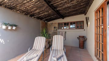 Une terrasse couverte avec deux chaises longues à rayures, une plante en pot et un plafond en bois rustique.
