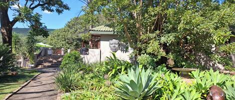 A garden with a pathway leading to a building with a green roof and a statue.