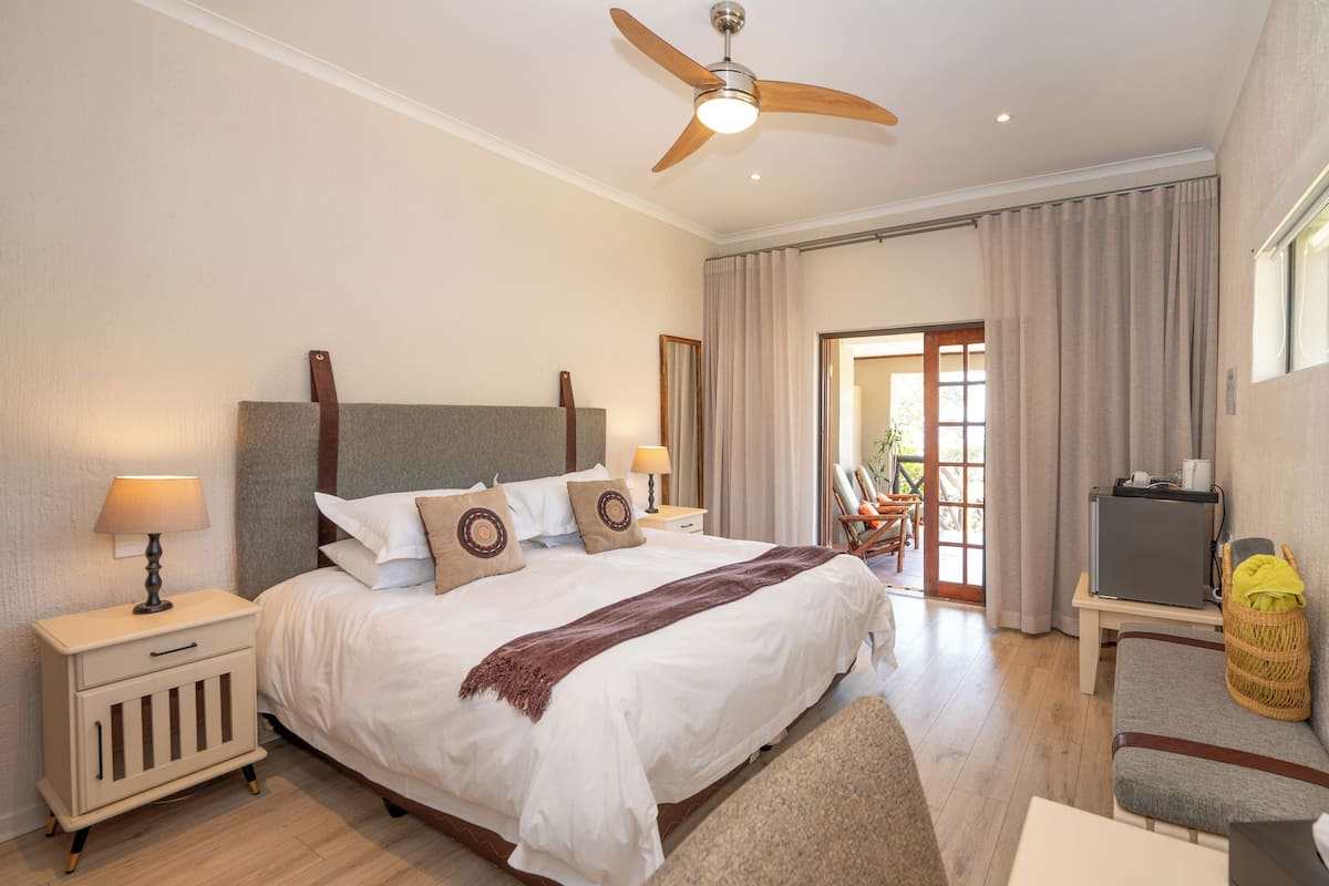A well-lit bedroom with a large bed, bedside lamps, a ceiling fan, and a view of the outside through a glass door.