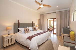 Un dormitorio bien iluminado con una cama grande, lámparas de noche, un ventilador de techo y vistas al exterior a través de un ventanal.