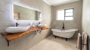 Een badkamer met een houten wastafelmeubel, twee wastafels, een grote spiegel, een vrijstaand bad en een raam.