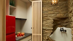 Eine kleine Küche mit einem roten Kühlschrank, einer Trennwand aus Holzleisten, einer Steinwand und einem kleinen Spülbecken mit einer dekorativen Figur.