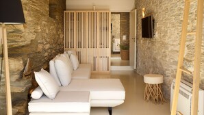 Ein modernes Interieur mit Steinwand, weißem Sofa mit Kissen, Holzboden und Wand-Fernseher.