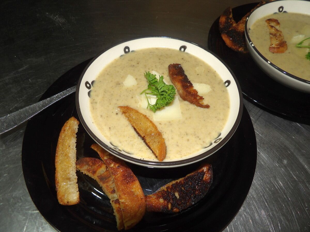 Una ciotola di zuppa con pane su un piatto nero.