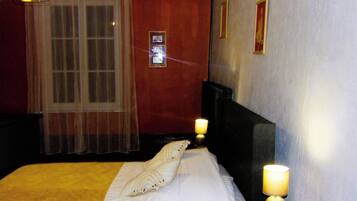 A hotel room with a bed, two bedside lamps, a window with sheer curtains, and a wall with framed pictures.