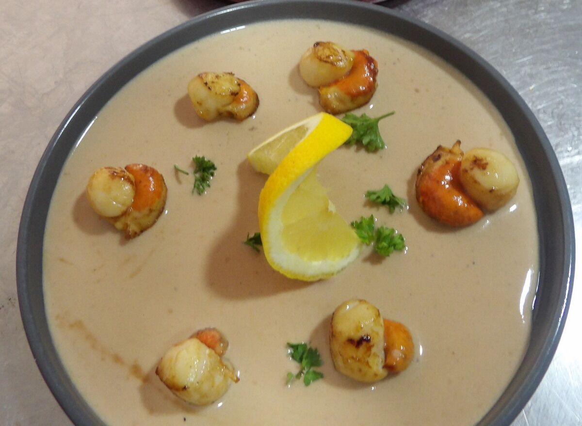 A bowl of creamy soup with seared scallops and lemon garnish.