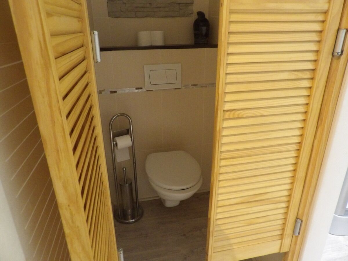 Un baño pequeño con inodoro, dispensador de papel higiénico y un estante con artículos de aseo.